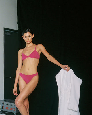 Woman in a pink bralette and panties standing against a black background
