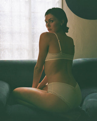 Woman in white lingerie sitting on a couch with soft lighting