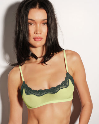 Woman wearing a green bralette with lace trim against a plain background